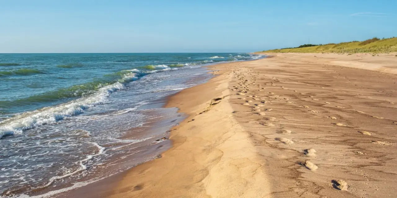 Spokojne, dzikie plaże nad Bałtykiem. Fale delikatnie obmywają piaszczysty brzeg, a na piasku widoczne są ślady stóp.