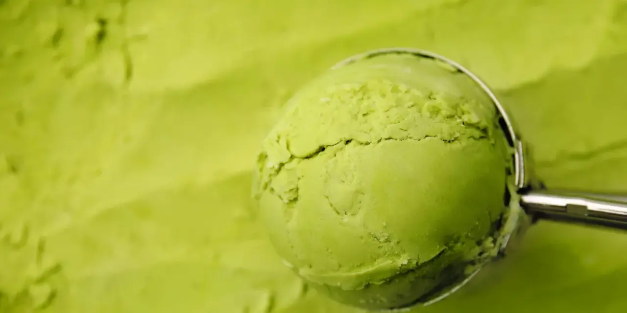Eine Kugel cremiges Matcha-Eis wird mit einem Löffel aus einer Schüssel gehoben. Perfekt für ein erfrischendes Matcha Eis Rezept.