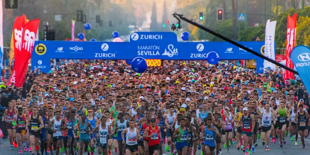 Multitudinaria salida del maratón Sevilla 2026, con miles de corredores bajo el arco de meta.