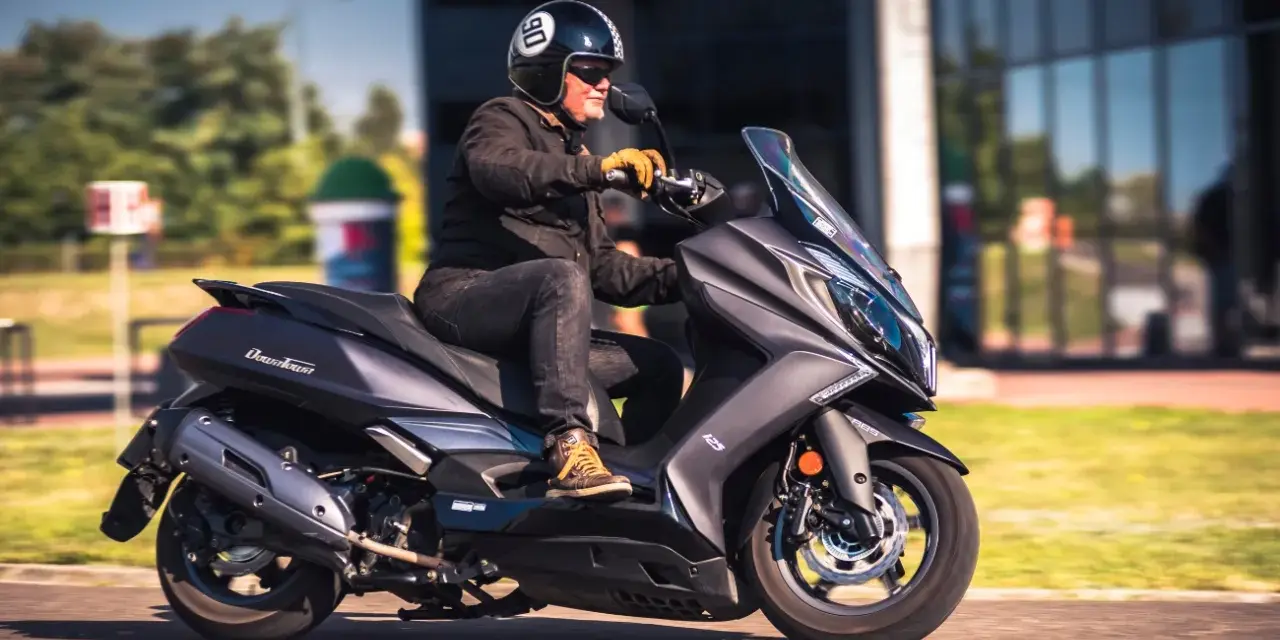 Mężczyzna w kasku jedzie na skuterze Kymco Downtown 125. Poznaj kymco downtown 125 dane techniczne.