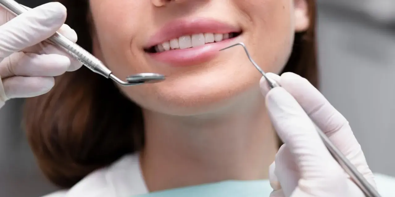 Uśmiechnięta kobieta podczas zabiegu remineralizacji szkliwa. Dentysta używa lusterka i sondy.