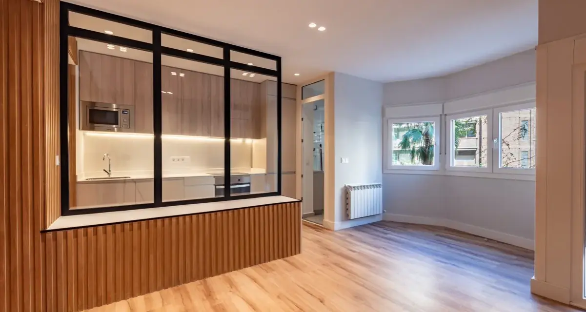 Entrada salón recibidor integrado. Cocina moderna con cristalera y madera, conectada a un luminoso salón con ventanas.