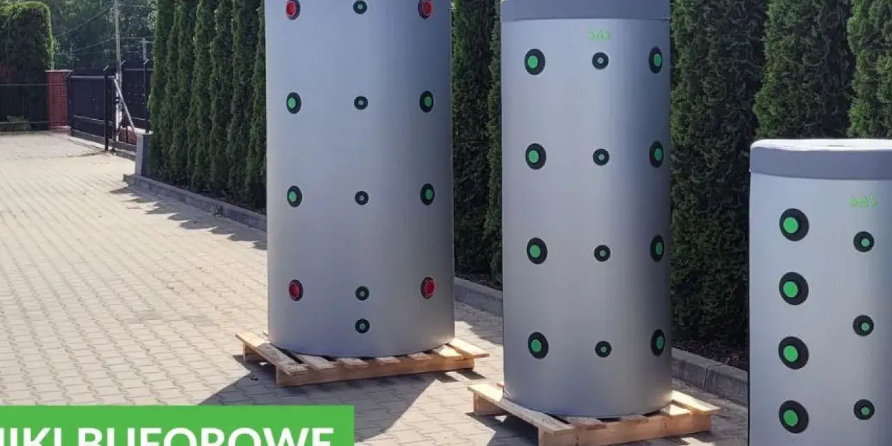 Trzy cylindryczne bufory 1000l wymiary, stojące na paletach przed żywopłotem. Zielone i czerwone kółka na szarych zbiornikach.
