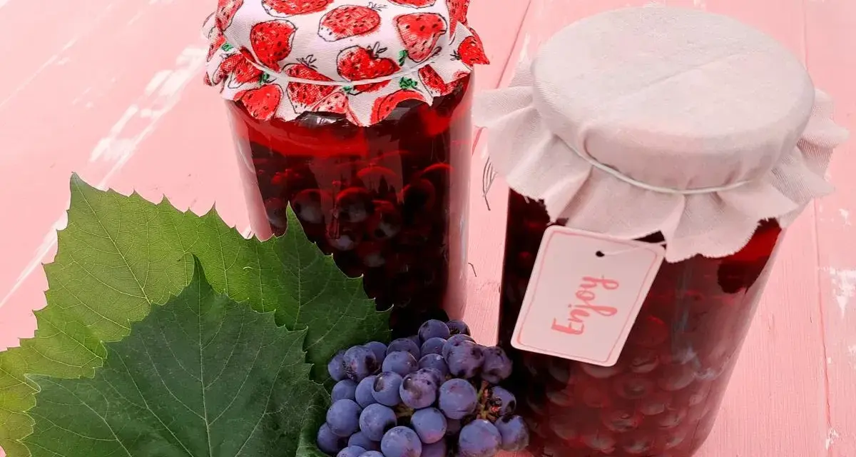 Słoiki z przetworami z winogron, przypominającymi wino z mrożonych winogron. Obok kiść winogron i liście.
