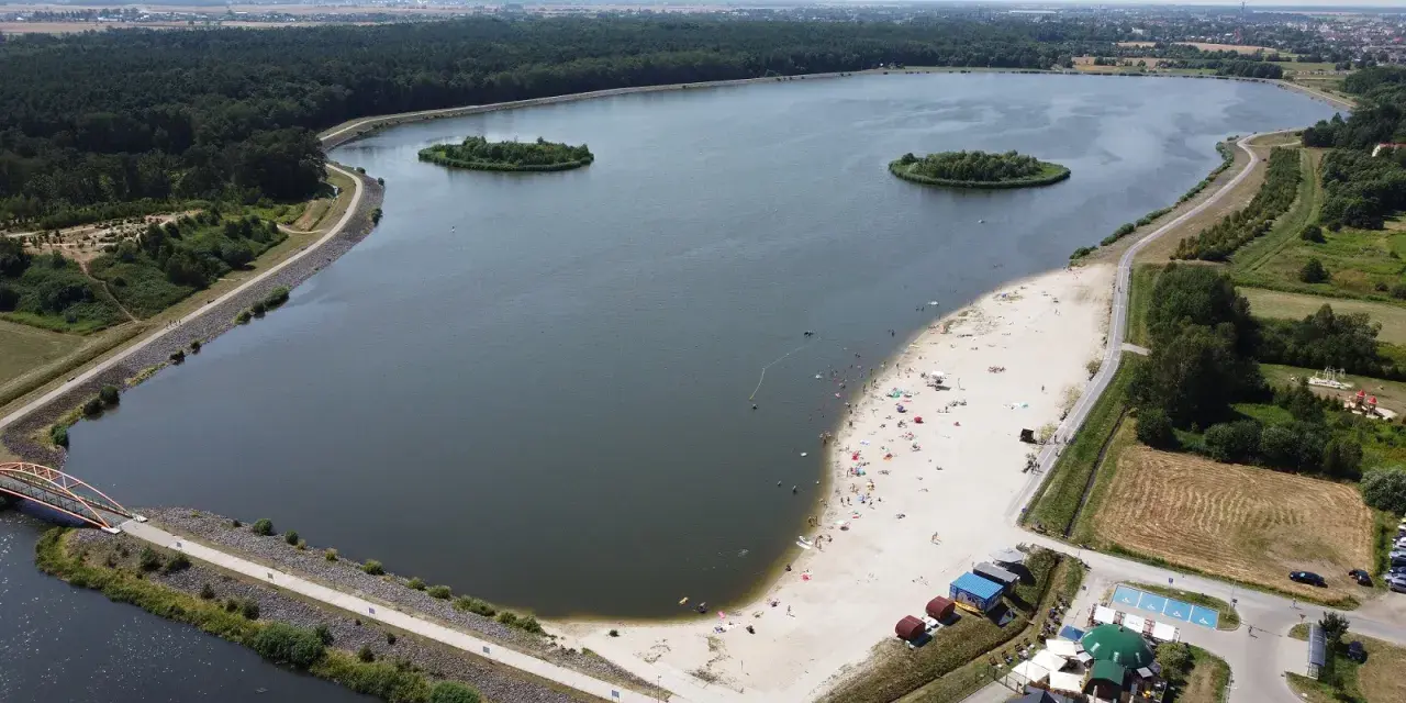 Opolskie atrakcje: piaszczysta plaża nad jeziorem, wyspy, las i mostek. Ludzie odpoczywają i kąpią się.
