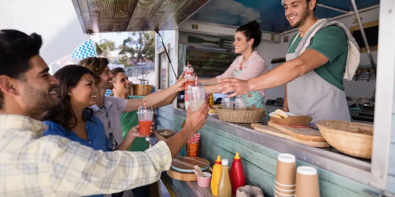 Uśmiechnięci ludzie odbierają napoje od barmanów z food trucka.