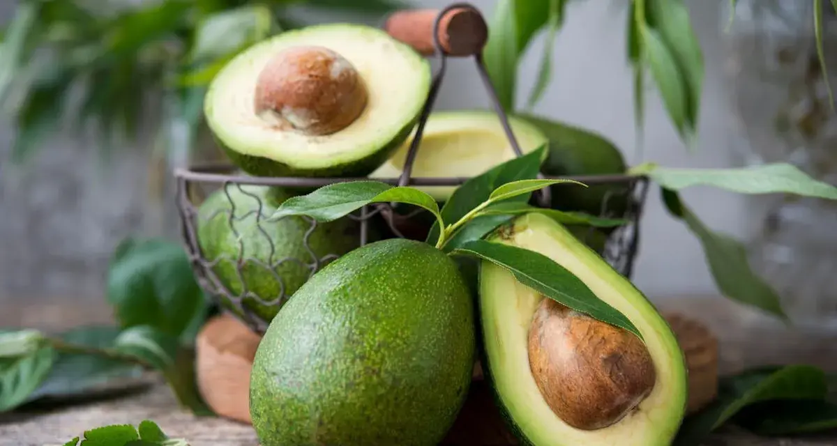 Des avocats frais, entiers et coupés en deux, dans un panier. Pour savoir comment avoir un avocatier qui donne des fruits, il faut de la patience et de bons soins.