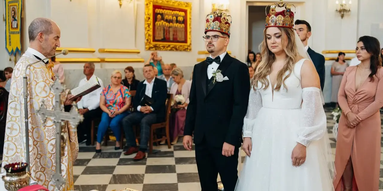 Uroczystość zaślubin w cerkwi. Pan młody, niczym ludowy grajek z Ukrainy, w eleganckim czarnym garniturze, z narzeczoną w białej sukni, przyjmują błogosławieństwo.
