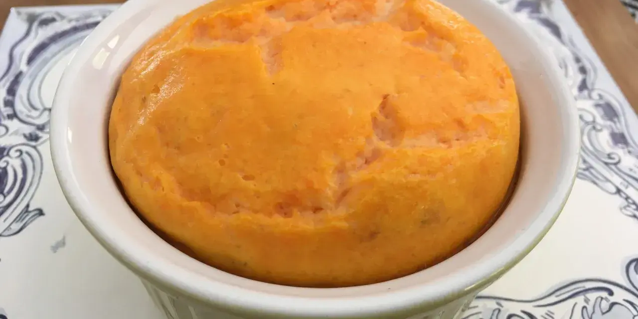 Un délicieux flan de carottes, doré et moelleux, servi dans un ramequin blanc sur une assiette décorée.