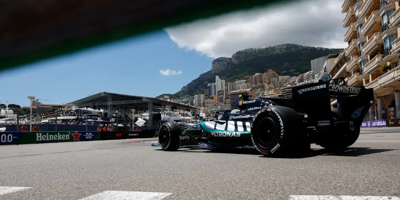 Coche de clasificación F1 en Mónaco, con el mar y edificios de lujo de fondo.