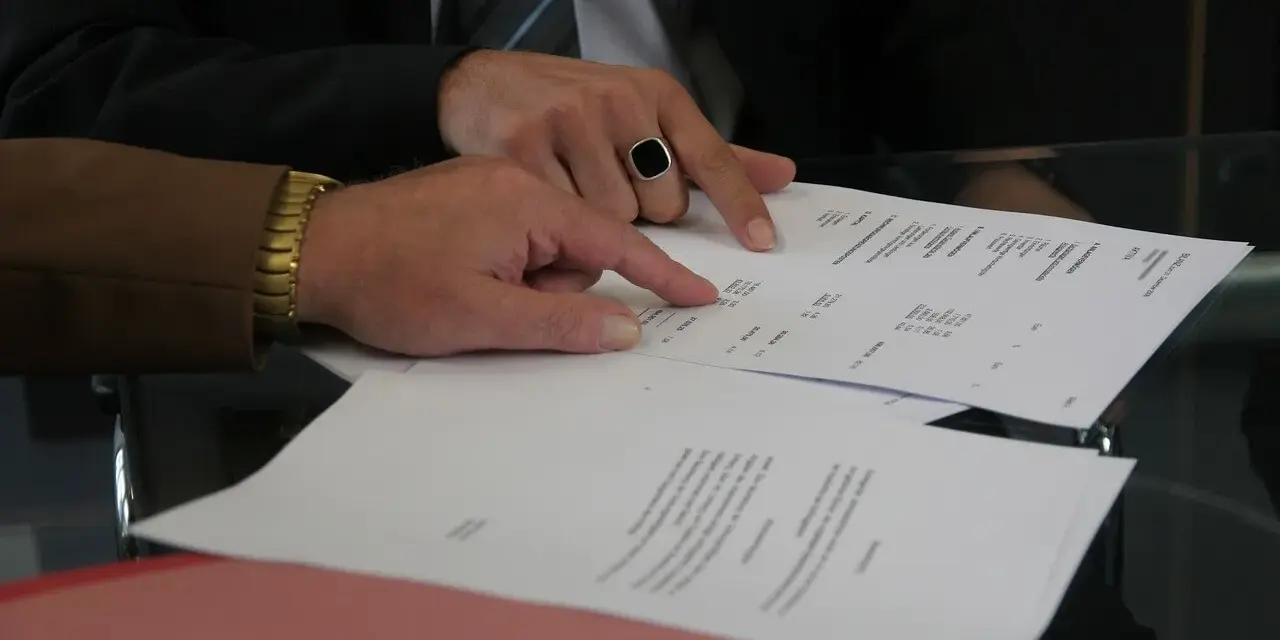 Dwóch mężczyzn analizuje dokumenty. Jeden z nich, w garniturze i z pierścieniem na palcu, wskazuje na tabelę. Pytanie: Millennium Bank zajęcie egzekucyjne jak sprawdzić?