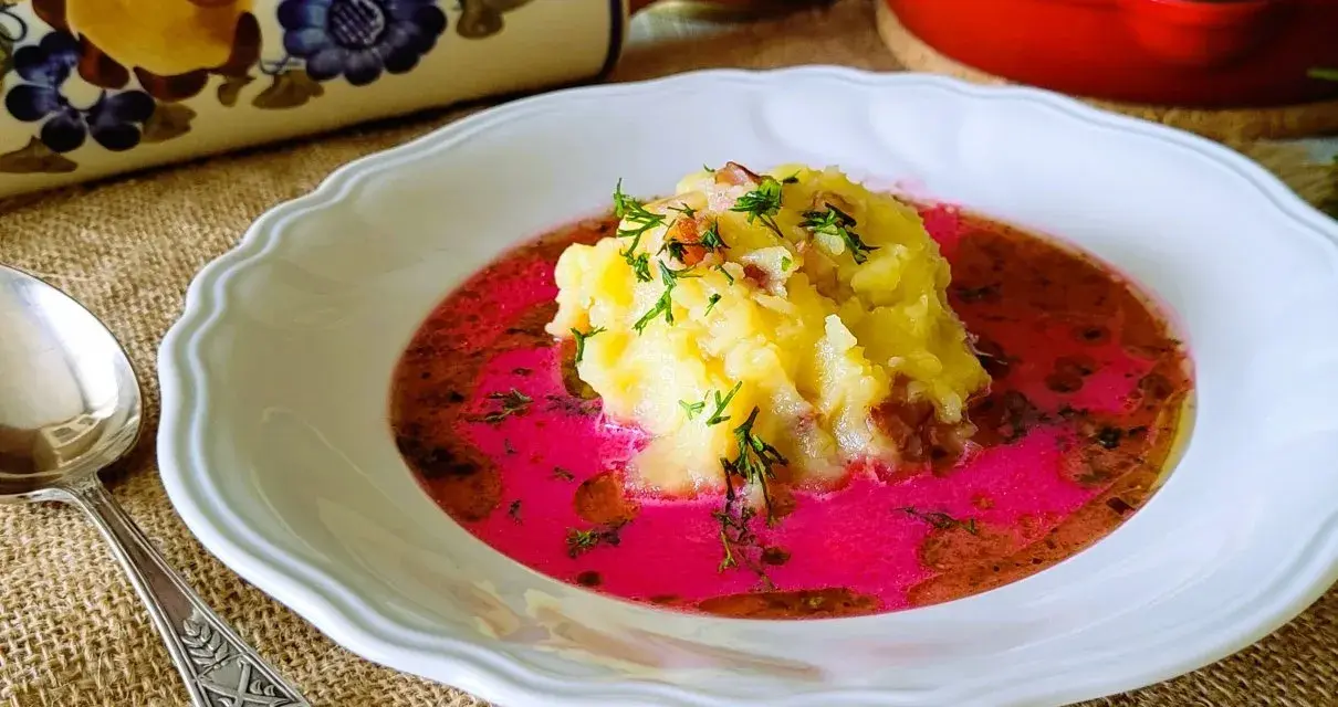 Pyszny barszcz czerwony zabielany, przepis babci. Na talerzu purée ziemniaczane z boczkiem i koperkiem w intensywnym, różowym barszczu.