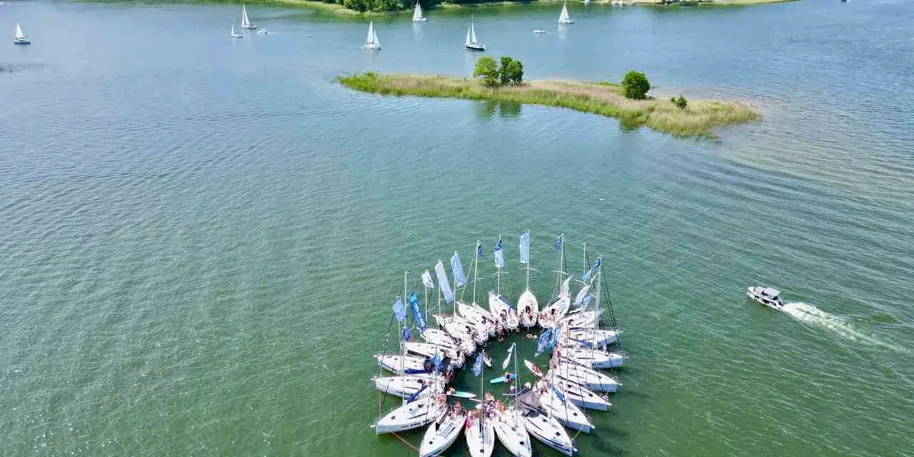 Żaglówki tworzą okrąg na jeziorze, otoczone lasem. To jedne z najpiękniejszych miejsc w Polsce – Mazury.