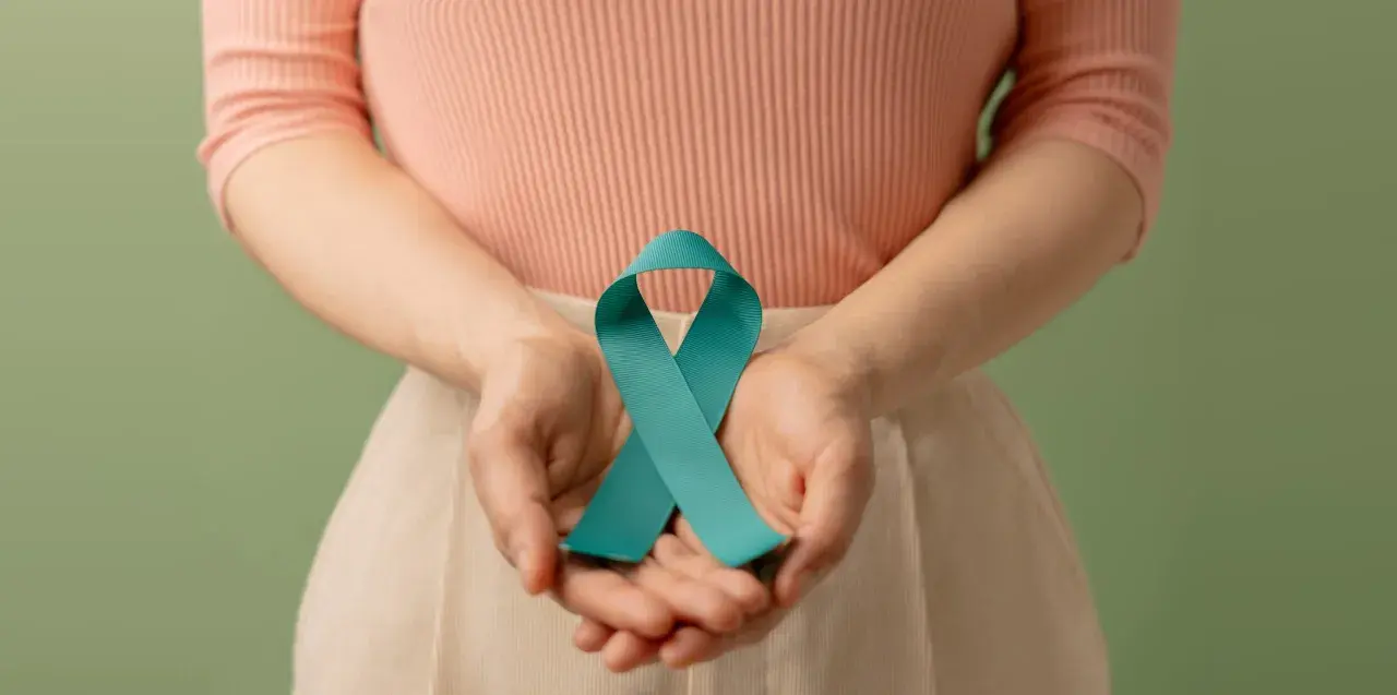 Dłonie trzymają turkusową wstążkę, symbolizującą wsparcie dla kobiet z PCOS. Dowiedz się, pcos co to.