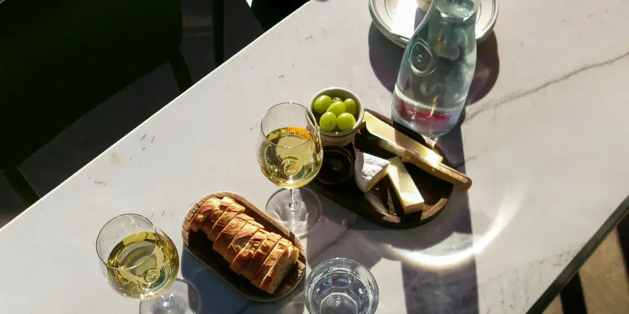 Dwa kieliszki orzeźwiającego gruner veltliner wino, chrupiąca bagietka, ser i winogrona na marmurowym stole.