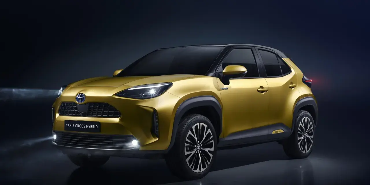 Złoty Toyota Yaris Cross Hybrid z włączonymi światłami na ciemnym tle.