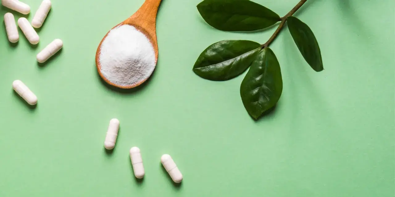 Vita C-vitaminer i kapslar och pulver på en sked, med gröna blad.