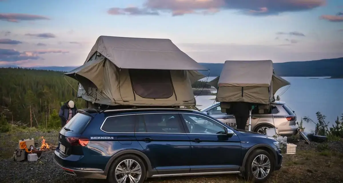 Två bilar med takboxar som fungerar som tält står redo för camping vid en sjö. En eld sprakar i förgrunden. En perfekt plats för camping i Gnesta.