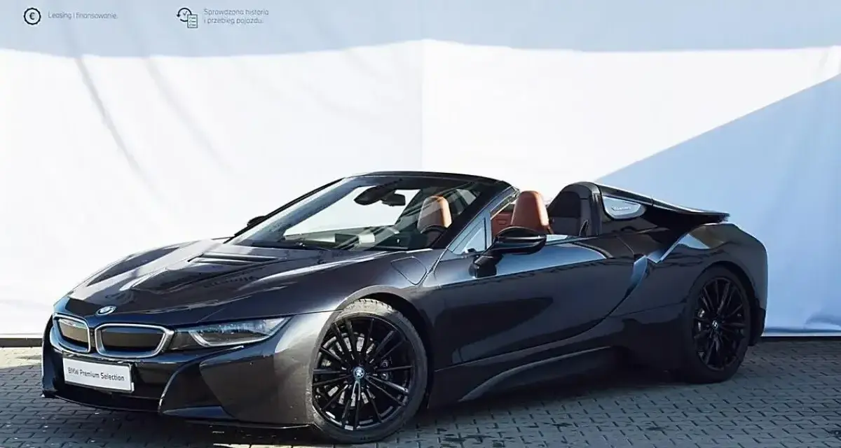 Ciemnoszary kabriolet BMW i8 z brązowym wnętrzem na tle białej ściany z logo BMW.
