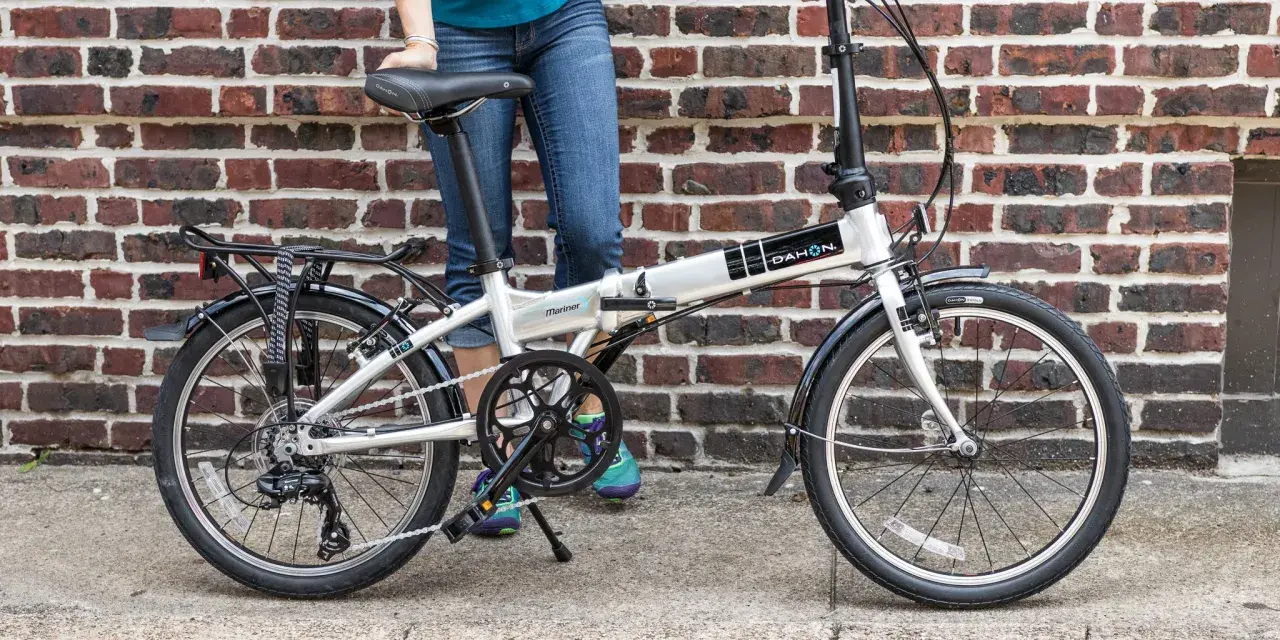 A person stands next to a silver Dahon Mariner folding commuting bike, ready for their next urban adventure.