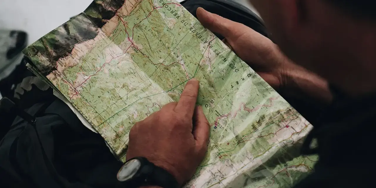 Un randonneur consulte une carte IGN des plateaux du Vercors, pointant un chemin sur le terrain.