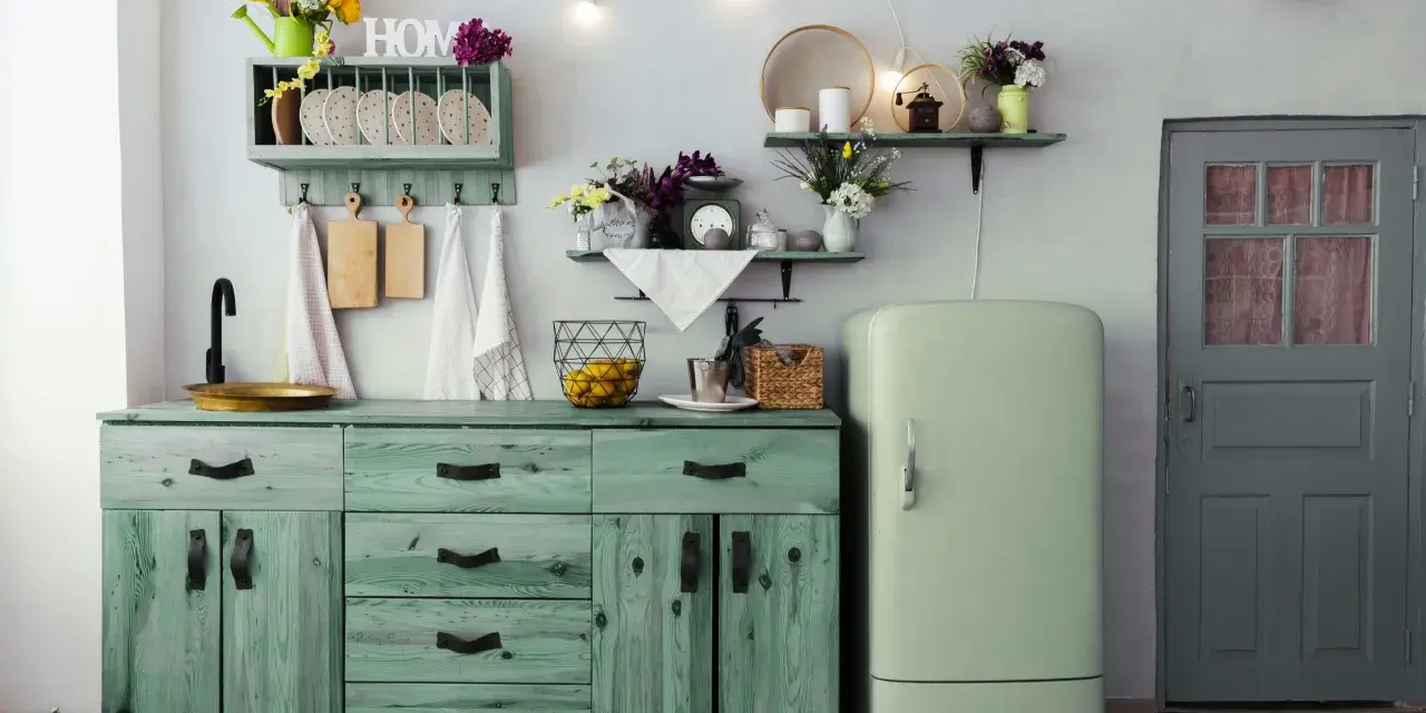 Cocina rústica con muebles de madera pintados en pintura a la tiza verde, un refrigerador vintage y una puerta gris.