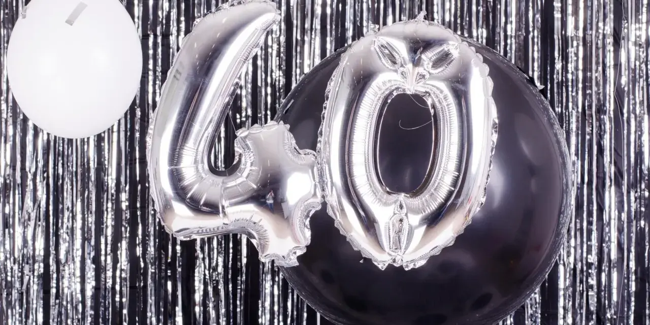 Srebrne balony z cyfrą 40 i biały balon na tle błyszczącej kurtyny. Idealne na zabawy na 40 urodziny!