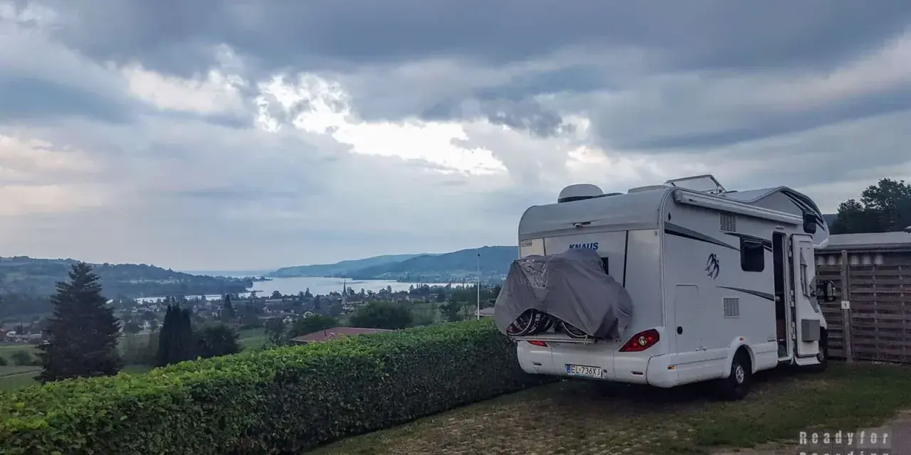 Kamper zaparkowany na kempingu w Czeskiej Szwajcarii, z widokiem na jezioro i wzgórza.