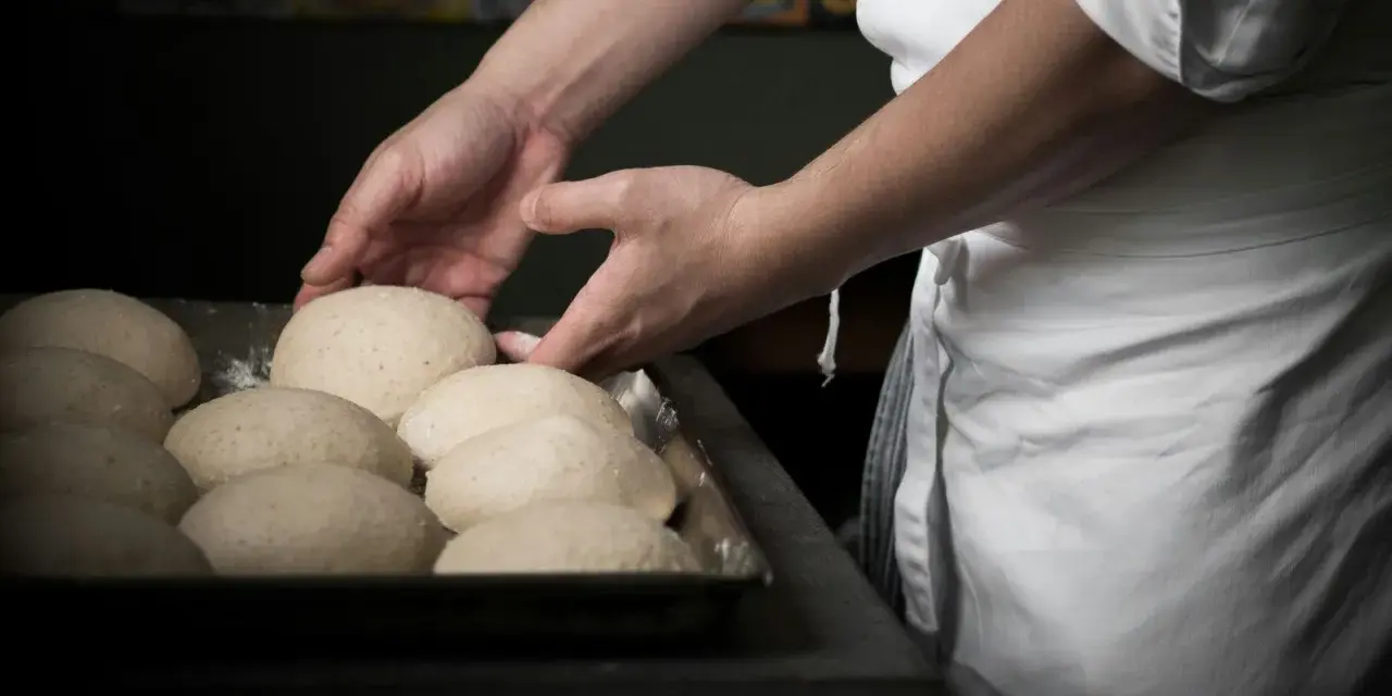 Mani esperte sistemano impasti per pizza, un mestiere che fa riflettere su quanto guadagna un pizzaiolo al mese.