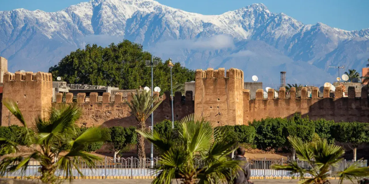 Marrakesz, gdzie leży, widać na tle ośnieżonych gór Atlas. Stare mury miasta i palmy tworzą malowniczy krajobraz.