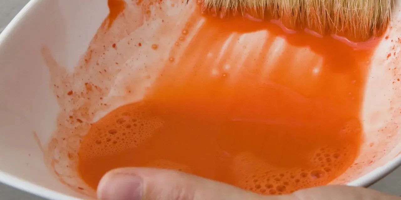 Maintenant, où jeter l'eau de rinçage des pinceaux ? Une main tient un bol blanc rempli d'eau orange trouble.