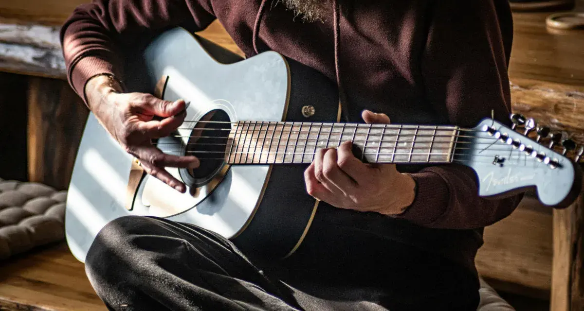Mann spielt Akustikgitarre, Hände auf Saiten und Plektrum.