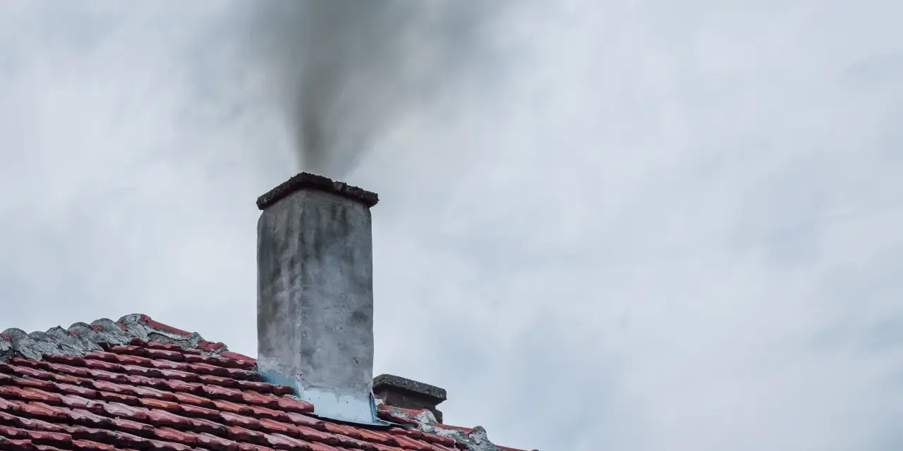 Dym wydobywający się z komina na tle pochmurnego nieba.