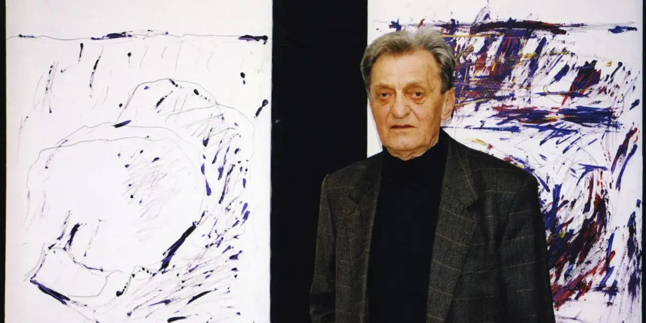 Jacek Sempoliński, artysta, stoi obok swoich abstrakcyjnych obrazów.