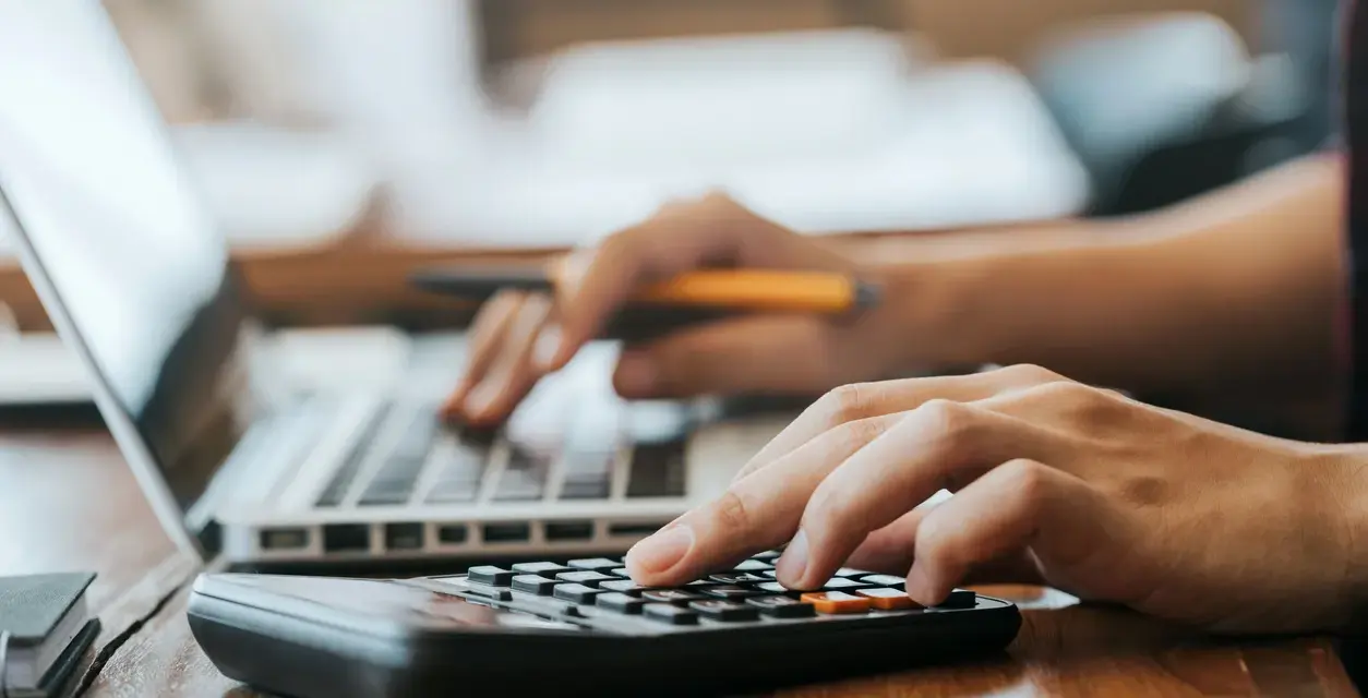 Hände bedienen Laptop und Taschenrechner. So lässt sich die Kaution in Raten zahlen und die Finanzen im Blick behalten.