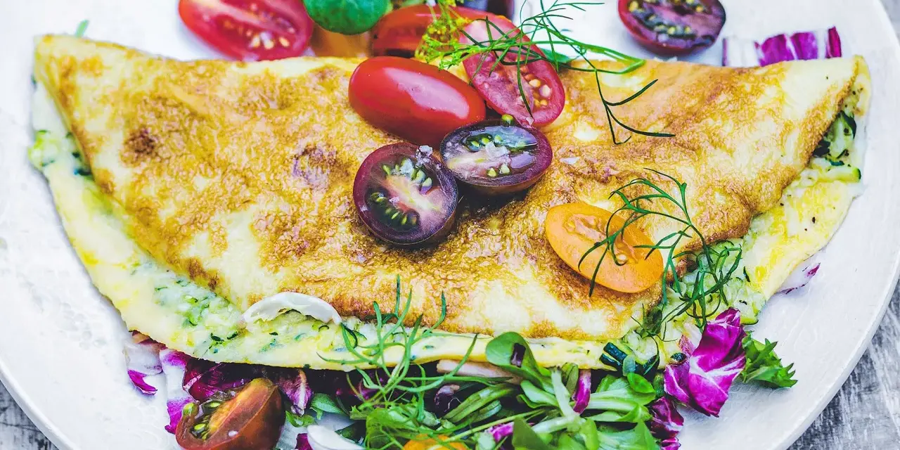 Złocisty omlet z cukinią, podany z kolorową sałatką i pomidorkami koktajlowymi. Pyszne i zdrowe śniadanie.