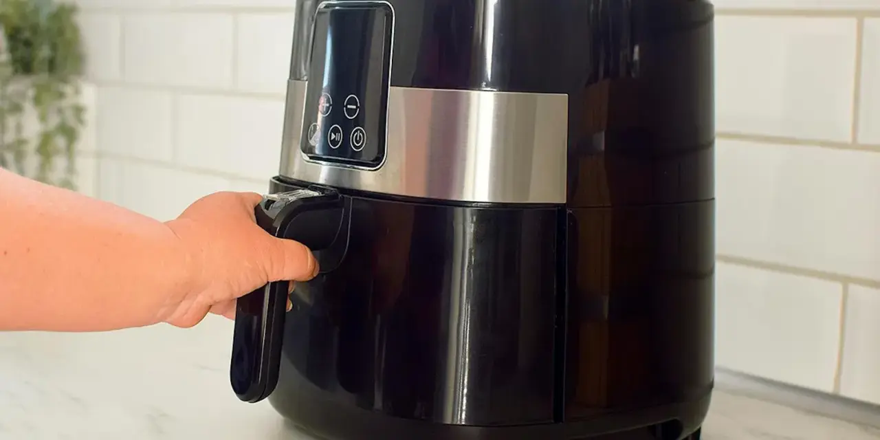 En hand drar ut korgen på en svart airfryer. Den här köksapparaten är lika praktisk som en diskmaskin för snabb matlagning.
