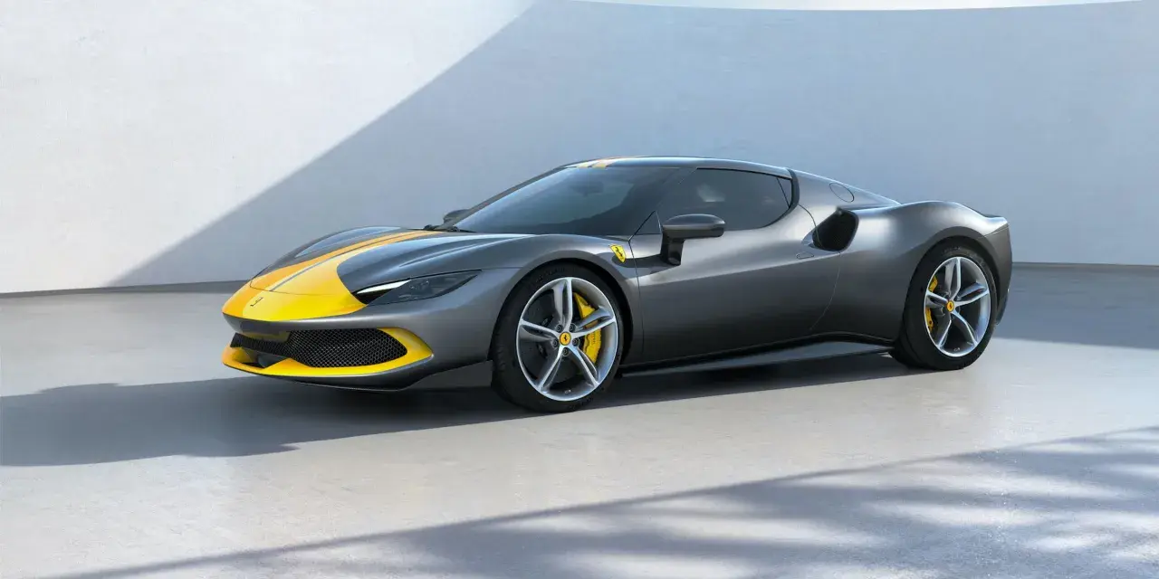 Szary Ferrari 296 GTB z żółtymi pasami na masce i dachu, stojący na betonowej posadzce.