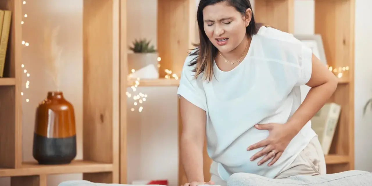 Frau mit schmerzverzerrtem Gesicht hält ihren Bauch, als ob sie Wehen erkennen würde.