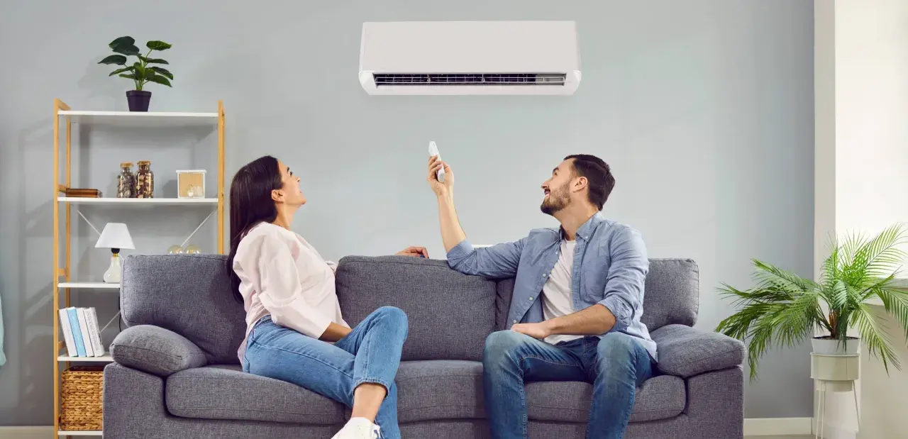 Pareja ajustando el aire acondicionado para encontrar la temperatura ideal y ahorrar energía.