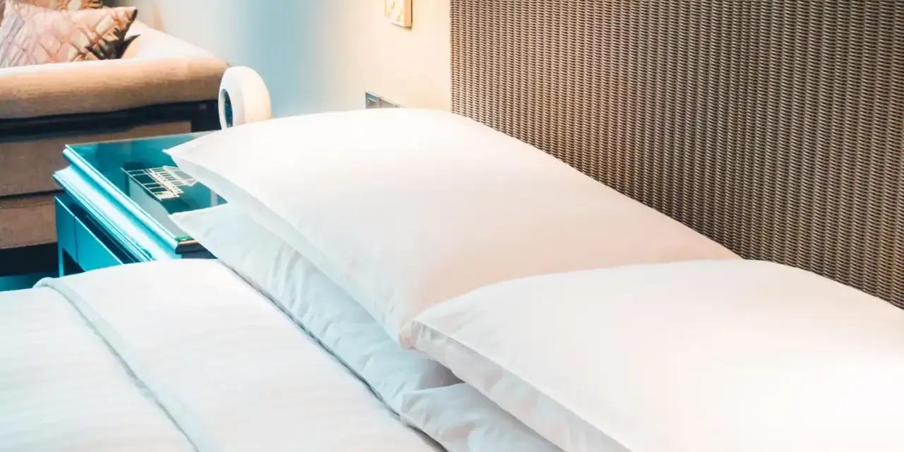 Cama de hotel con almohadas blancas y cabecero de mimbre. Una guía para saber como elegir un colchon.