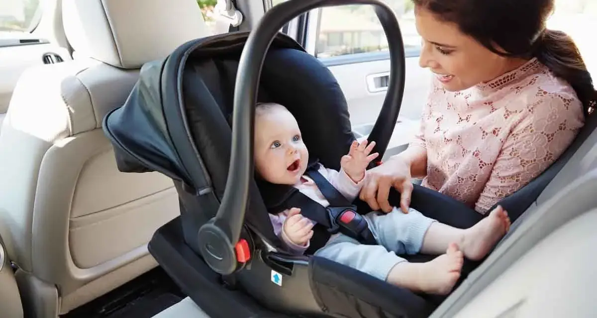 Uśmiechnięta mama patrzy na swojego **noworodka w foteliku samochodowym**, gotowego na podróż.