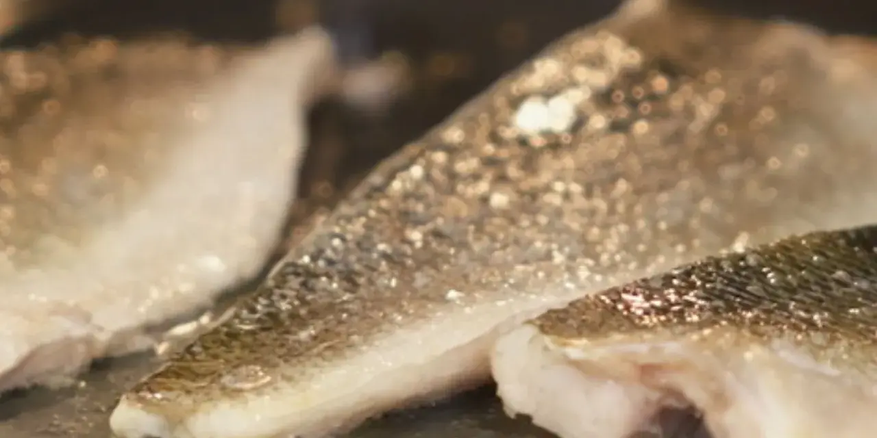 Filetes de lubina a la donostiarra dorándose en una sartén.