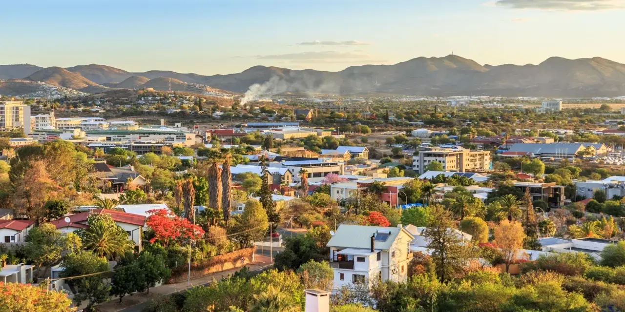 Widok na miasto Windhoek w Namibii o zachodzie słońca. W oddali góry, a bliżej zabudowania mieszkalne i komercyjne, otoczone bujną zielenią.