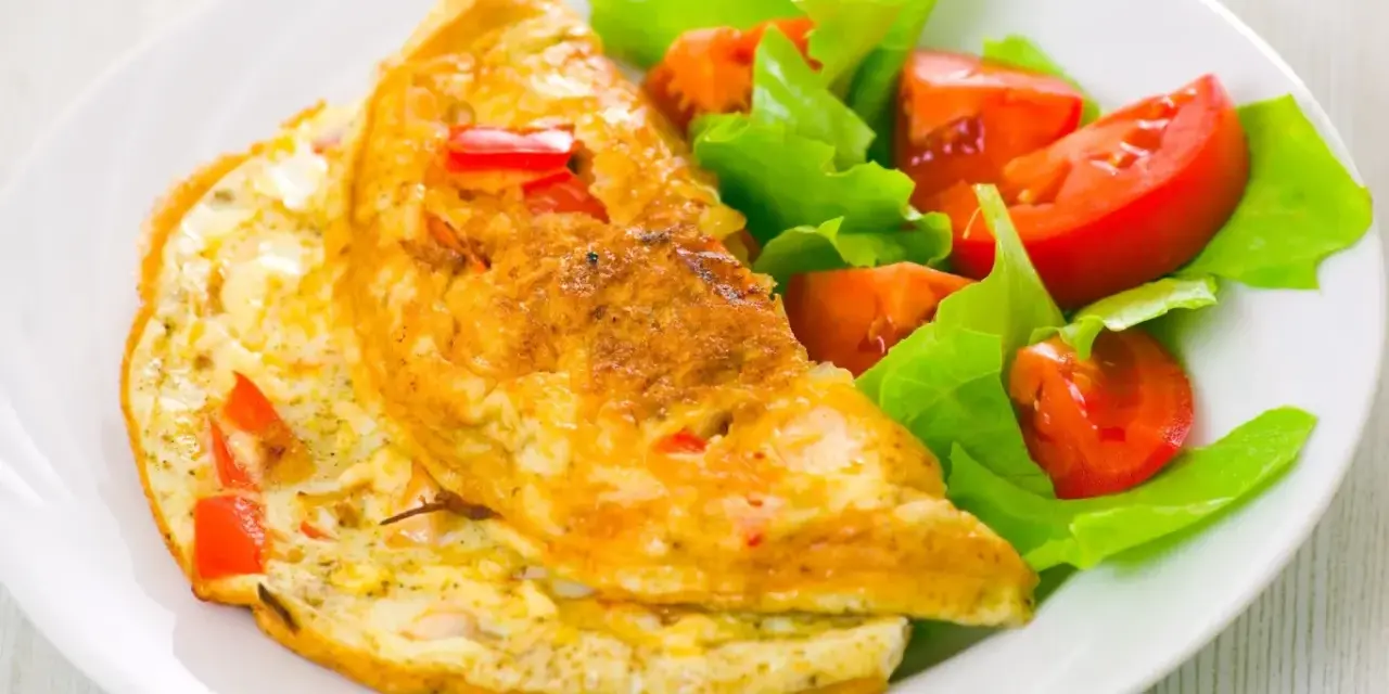 Złocisty omlet francuski z kawałkami papryki, podany z sałatką z pomidorów i sałaty. Pyszne śniadanie.