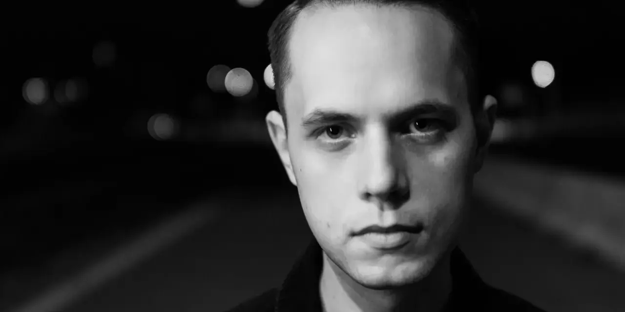 Młody mężczyzna, Gibbs producent, patrzy wprost w obiektyw na tle nocnych świateł.