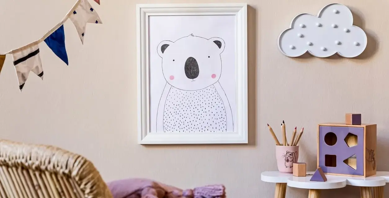 Adorable cuadros infantiles de un koala y una nube decoran la pared de una habitación. Una guirnalda de banderines alegra el ambiente.