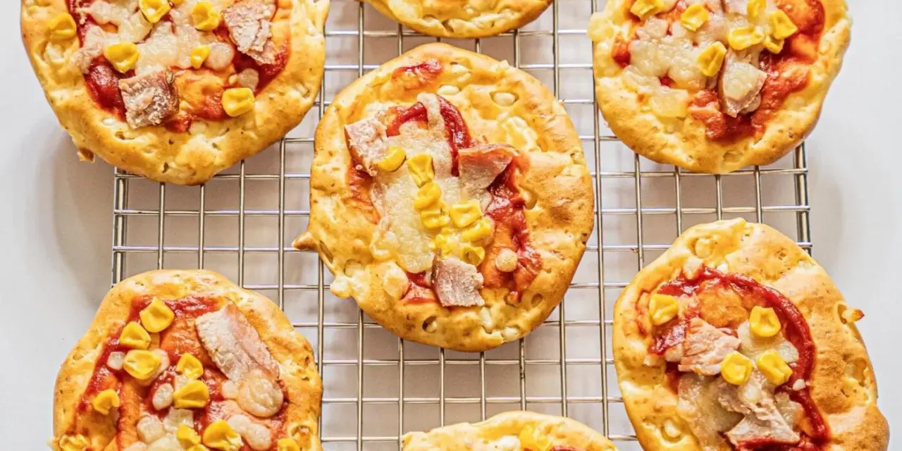 Mini pizze z serka wiejskiego, z kukurydzą i kawałkami mięsa, na metalowej kratce.