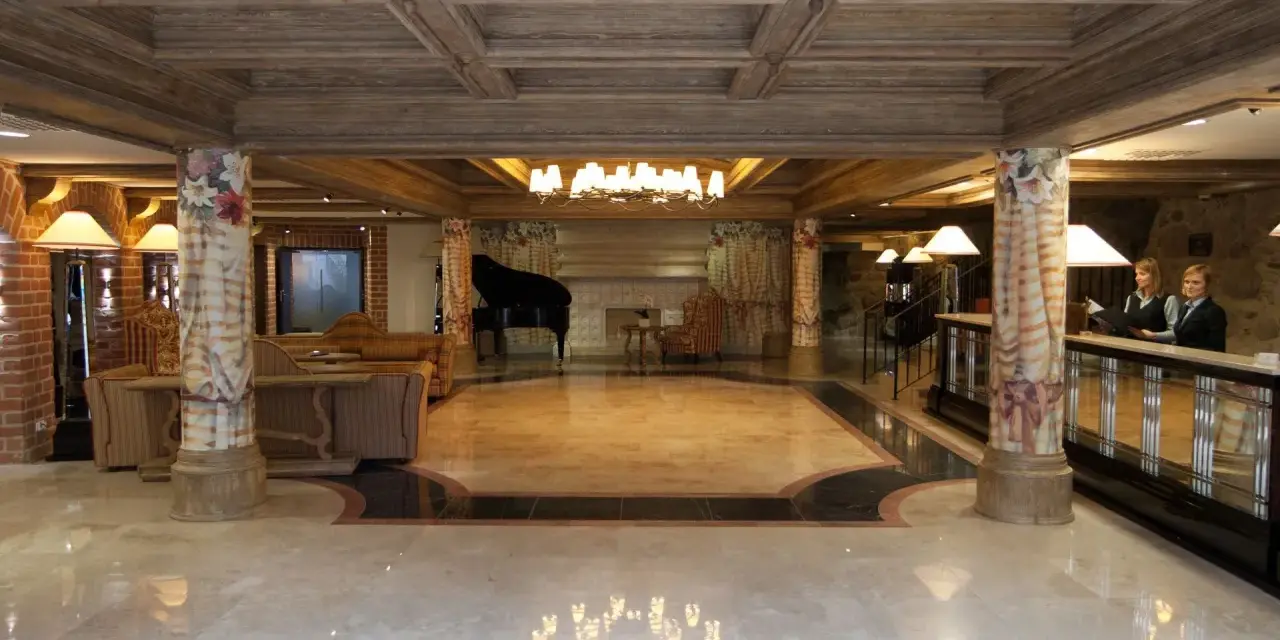 Eleganckie lobby hotelowe z fortepianem, recepcją i dwoma pracownikami.