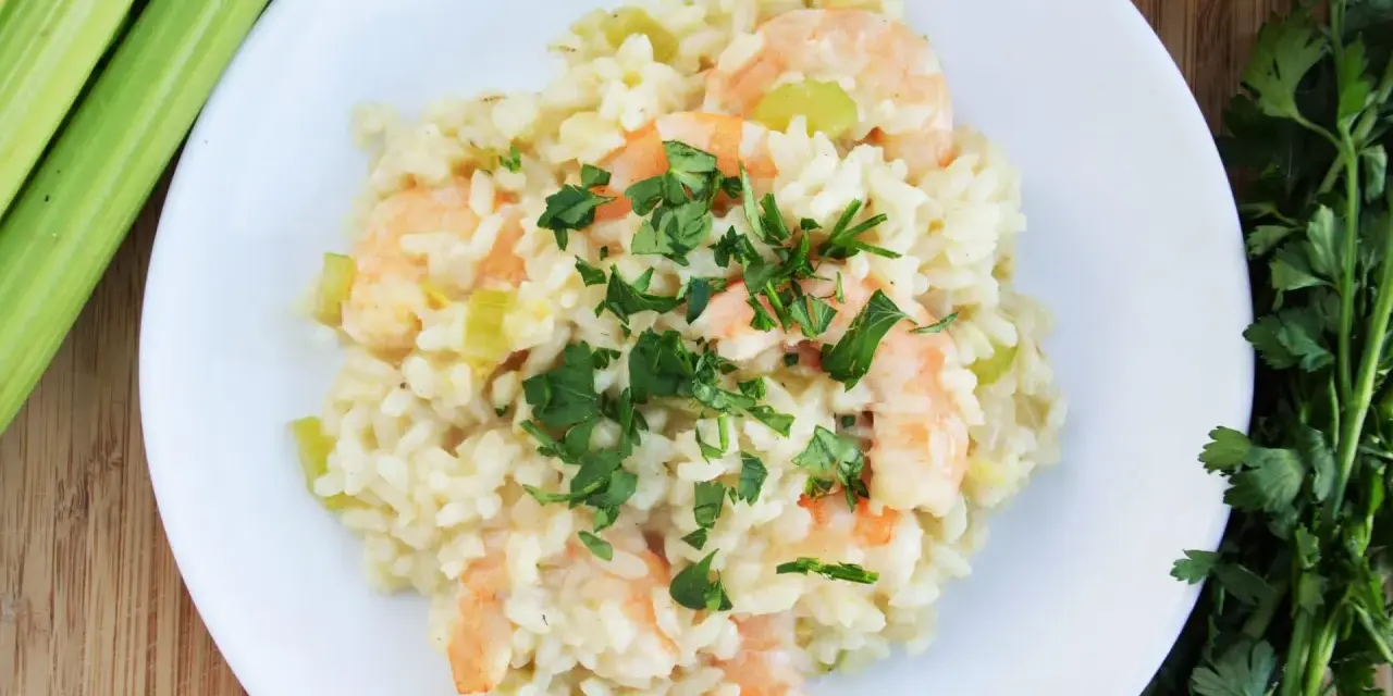 Kremowe risotto z krewetkami, ozdobione natką pietruszki, obok łodyg selera i oliwy.